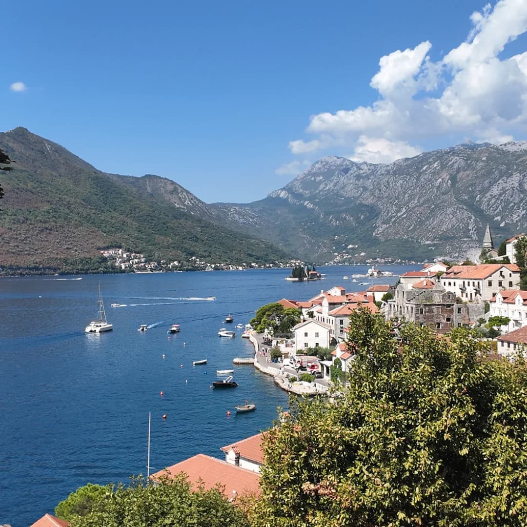 Perast seen from above, its single line of waterfront palaces along the shore with the two islets offshore in the bay.