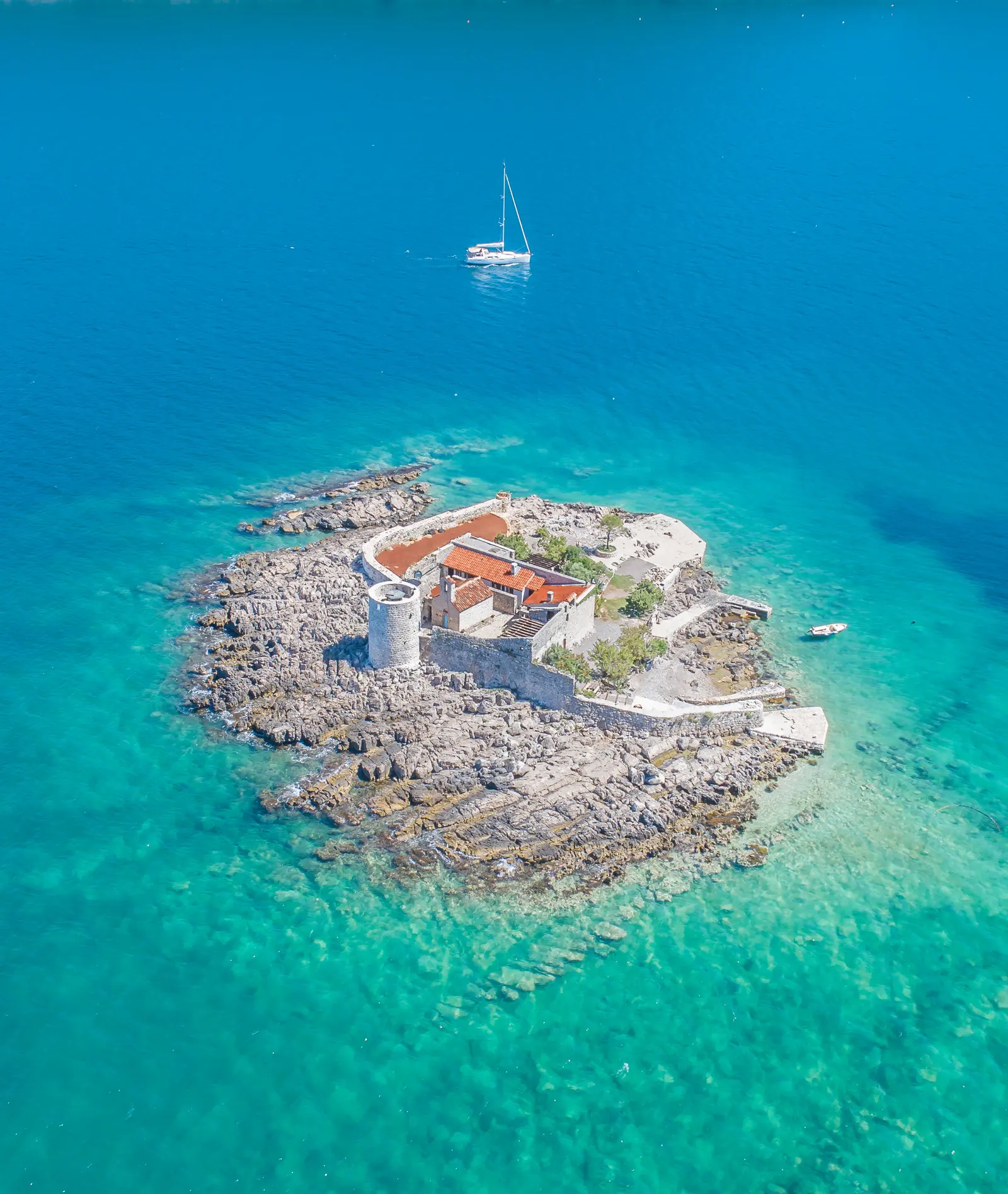 Aerial view of the walled Vavedenje monastery islet in clear water
