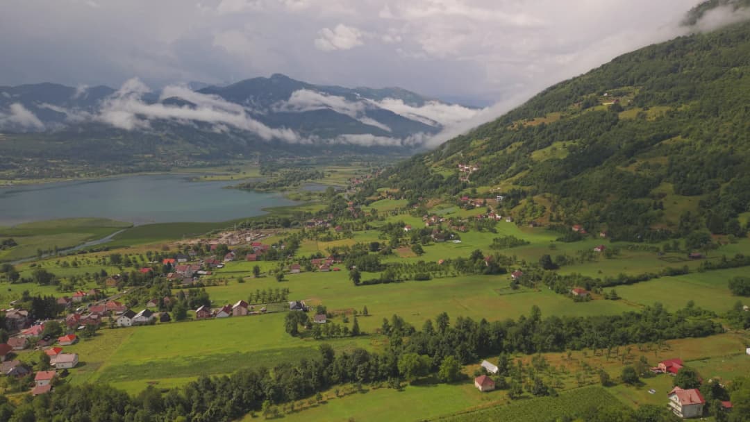 Pogled iz vazduha na plavsku dolinu, sa varoši i jezerskom kotlinom u obruču visokih planinskih padina.