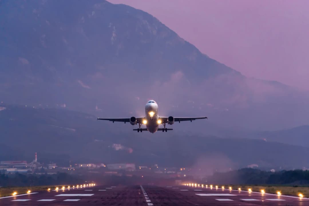 Zgrada terminala na tivatskom aerodromu, sa platformom piste ispred i planinama koje se uzdižu iza nje.