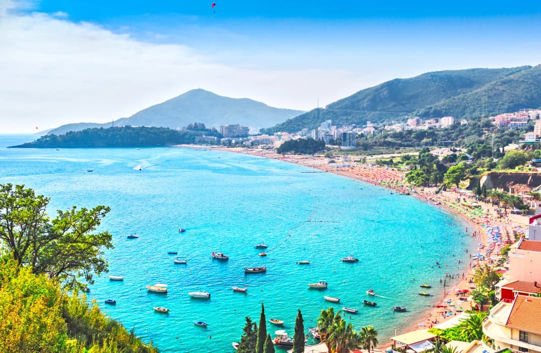 Pogled s visine na obalu Budvanske rivijere prema jugu, s nizom plaža i prepoznatljivom siluetom Svetog Stefana u daljini