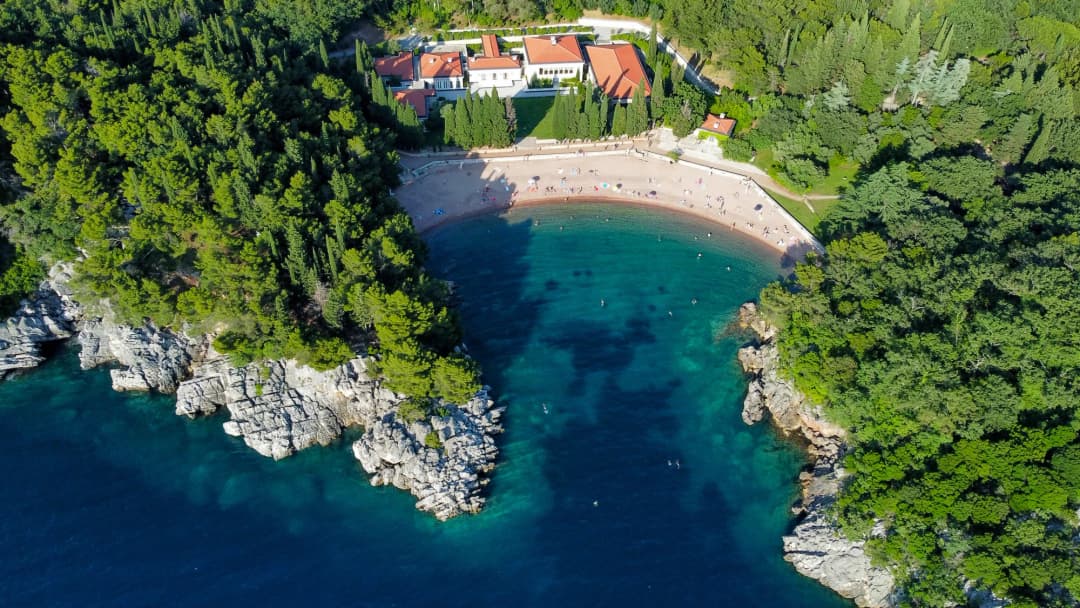 Kraljičina plaža u luku između pošumljenih rtova na miločerskoj obali, s ležaljkama na pijesku ružičastog tona.