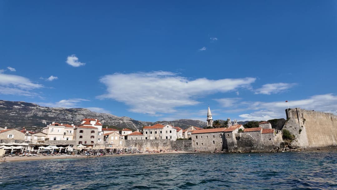 Stari grad Budve s mora kod Ričardove glave: morski bedem, Citadela zdesna i zvonik crkve Svetog Ivana iznad krovova.