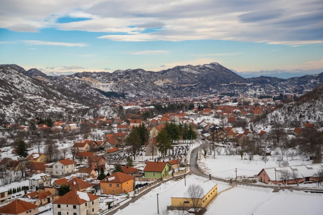 Spoljašnjost Cetinjskog manastira s kamenim zidovima i zvonikom, na planinskoj pozadini