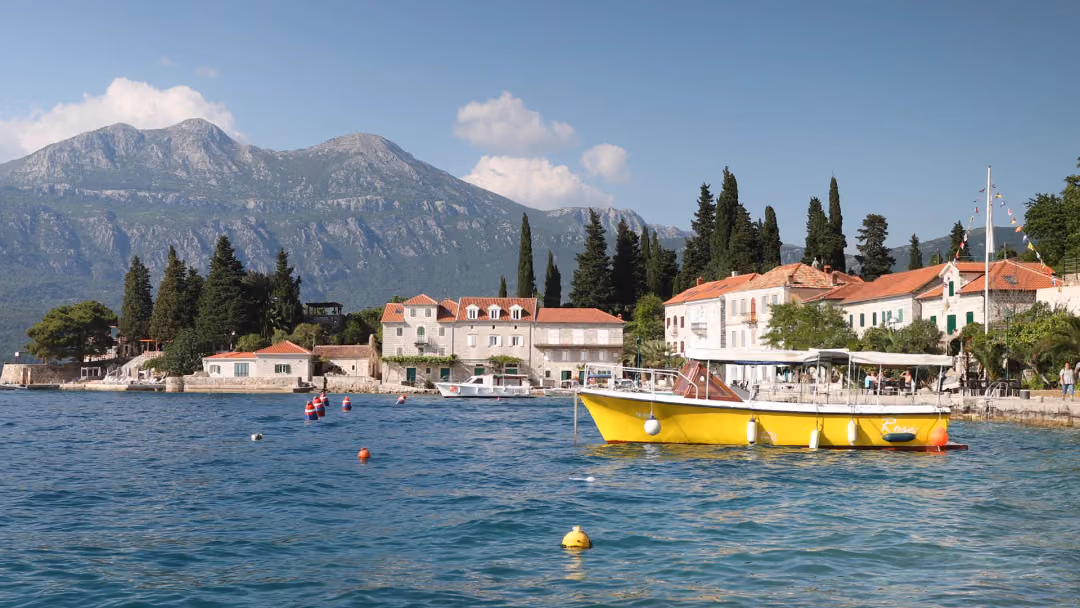 Rose waterfront, a yellow passenger boat and stone houses beneath the Orjen mountains