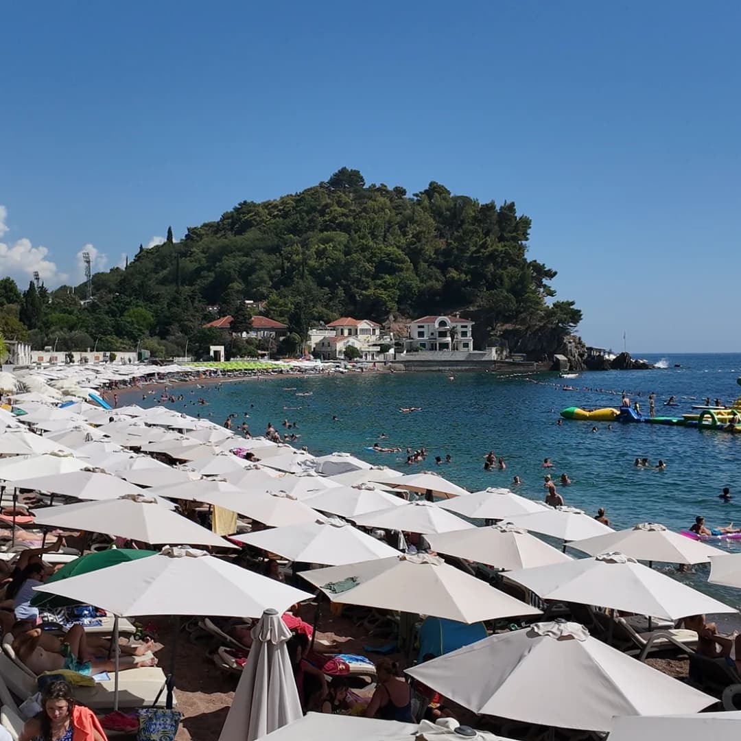 Redovi suncobrana na petrovačkoj plaži, s rtom koji zatvara njen dalji kraj.