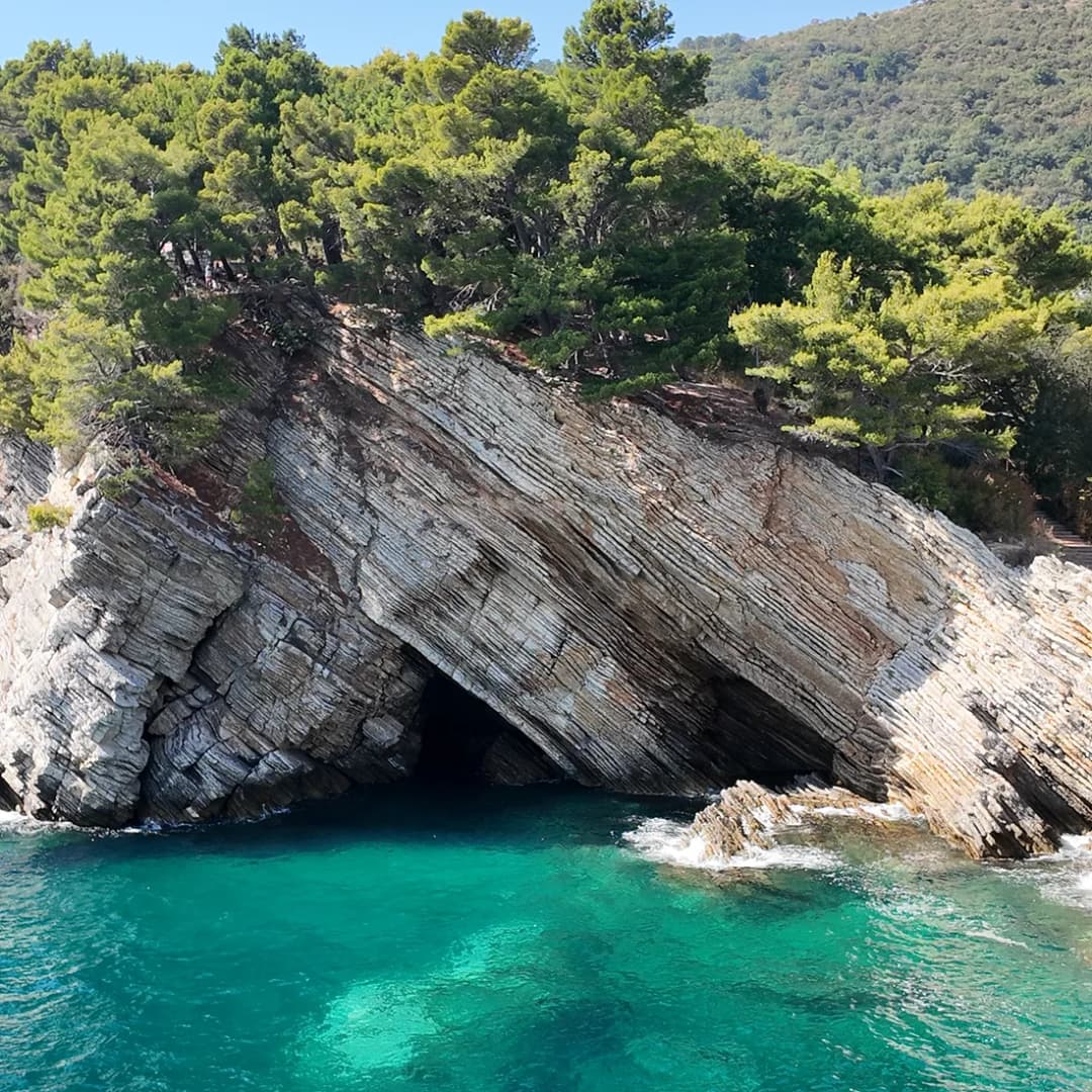 Niske stijene iznad bistre tirkizne vode, s morskom pećinom usječenom u kamen.