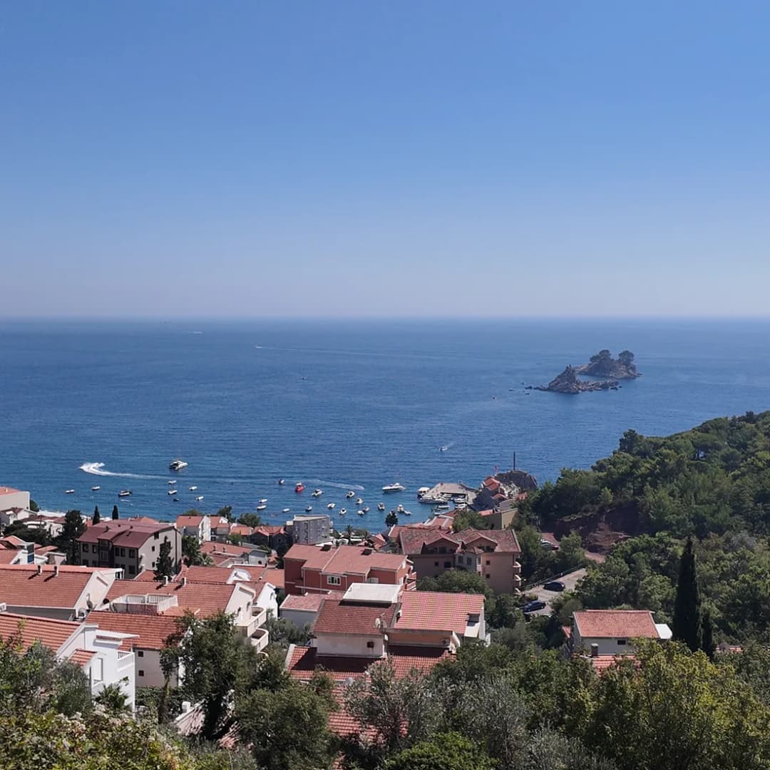 Kuće crvenih krovova u Petrovcu spuštaju se do lučice s malim čamcima, sa stjenovitim ostrvcem na pučini