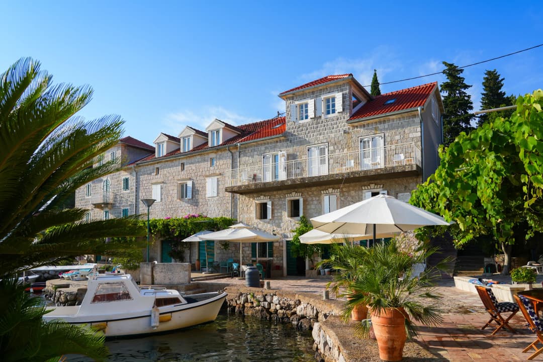 Traditional stone houses, palms and a small boat beside the water in Rose
