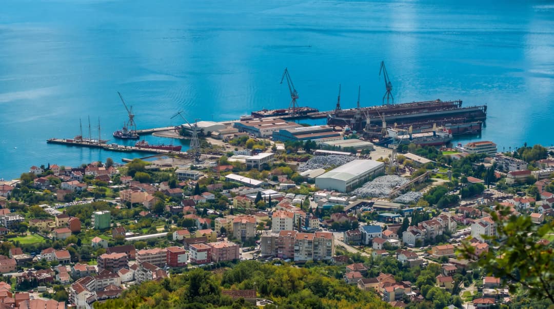 Aerial view of Bijela: the village rooftops in the foreground, the floating docks and cranes on the bay