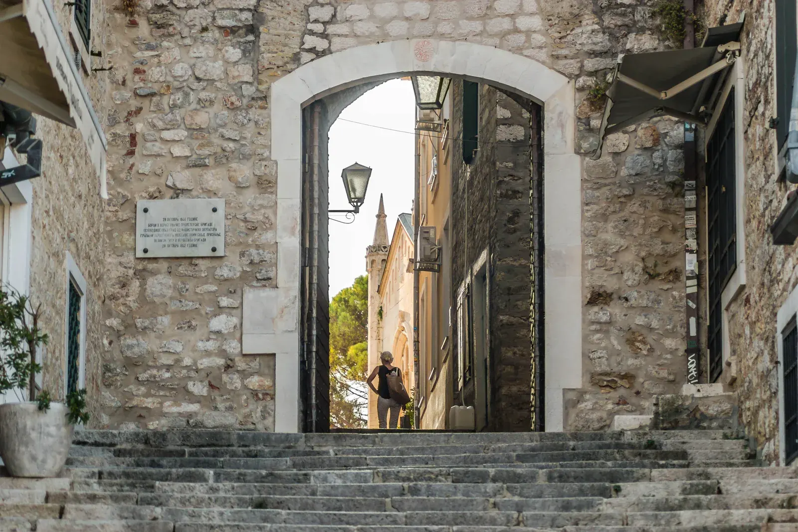 Una entrada al Casco Antiguo con arcos y escaleras de piedra en Herceg Novi, con una aguja de iglesia más allá