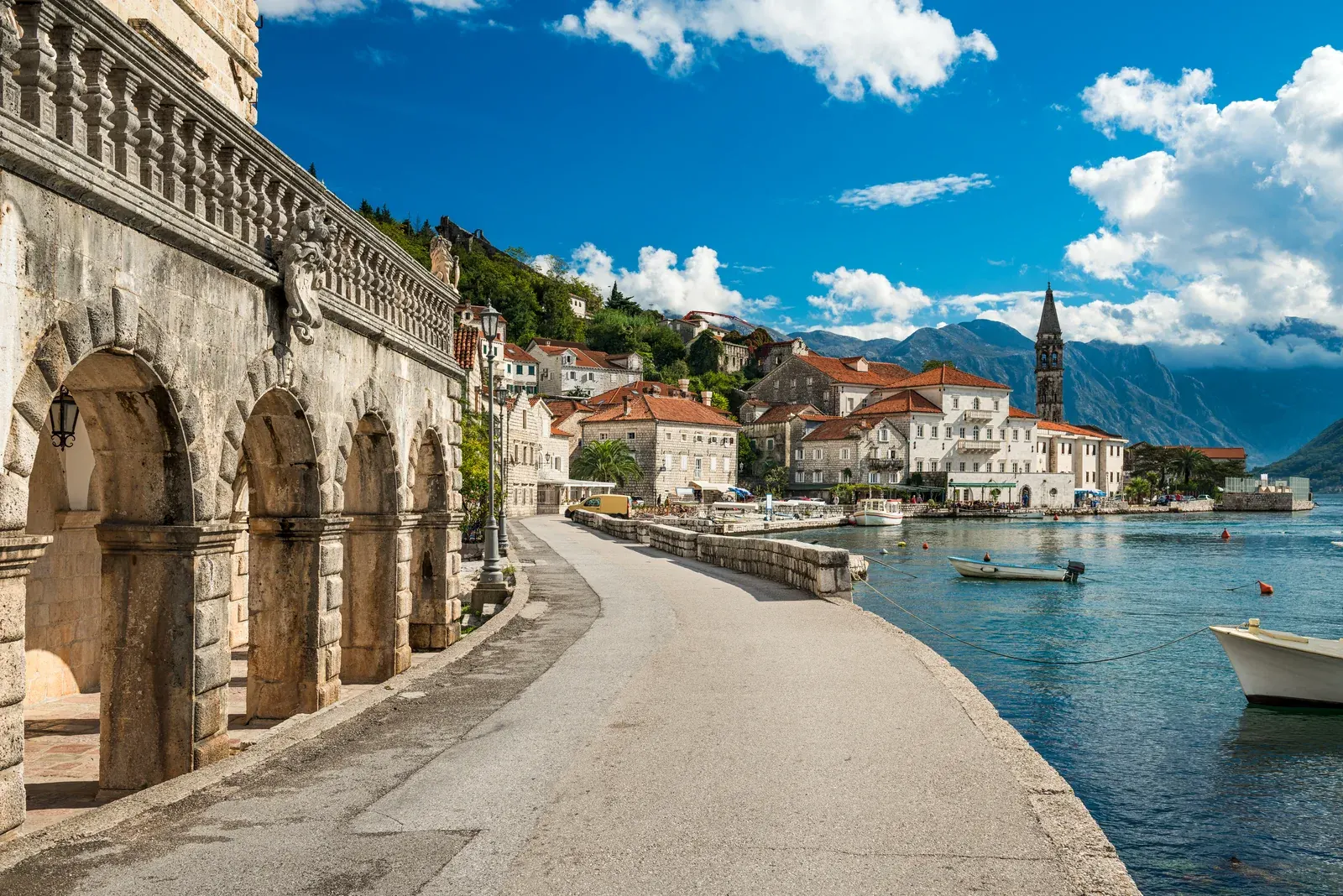 The arcaded stone palazzo and seafront promenade of Perast, with its tall bell tower and the bay