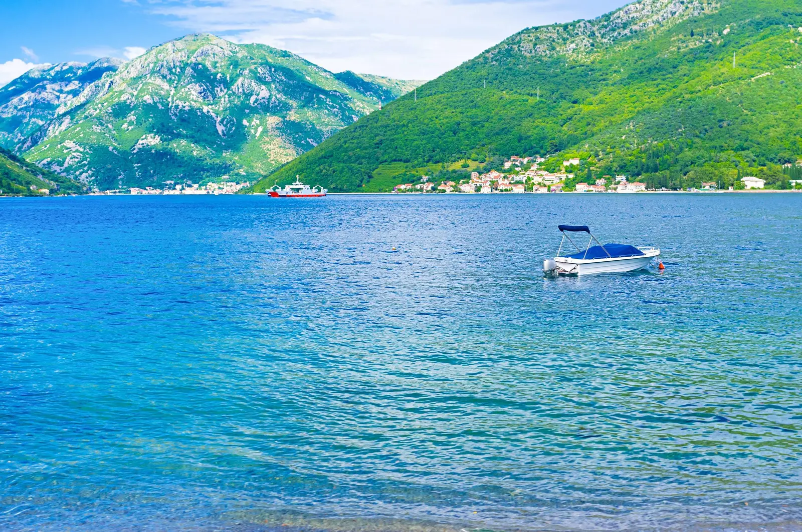 Mali čamac na mirnoj plavoj vodi zaliva ispod planina kod Kamenara